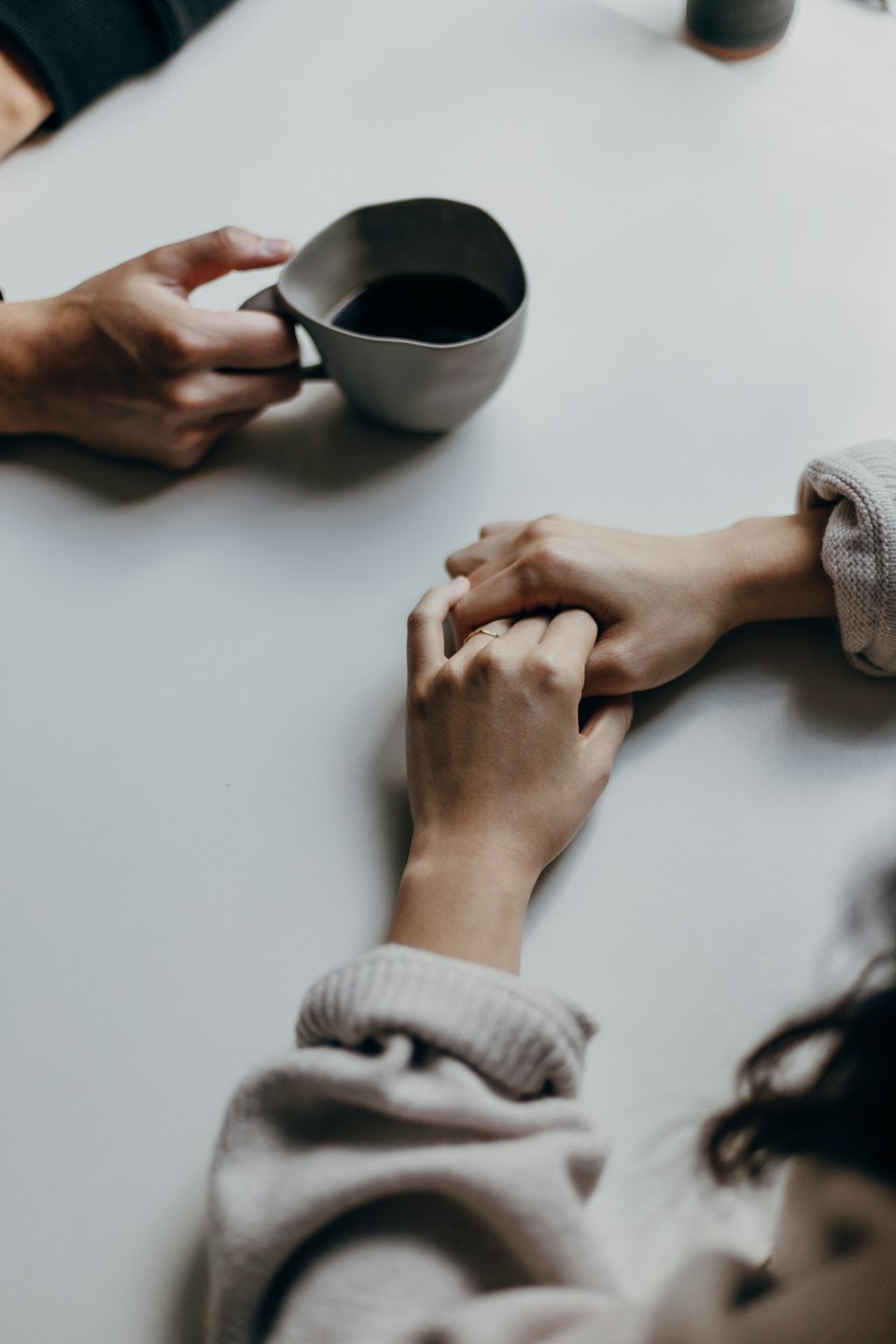 Two people hold hands over a coffee mug on a table.