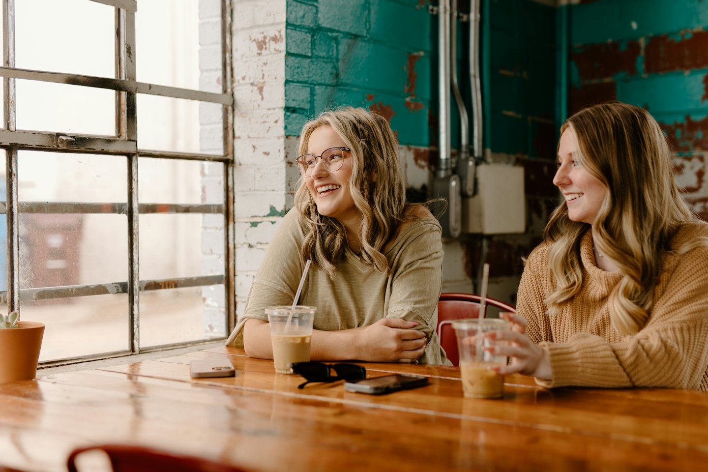 Two women chat and drink iced coffee at a cafe table.